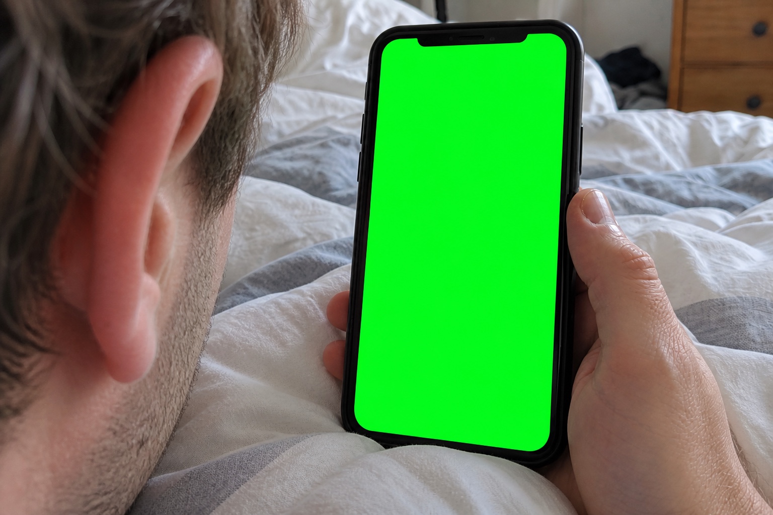 A candid close-up over a young man’s shoulder as he lies on his stomach in bed, chatting with Julia on his phone